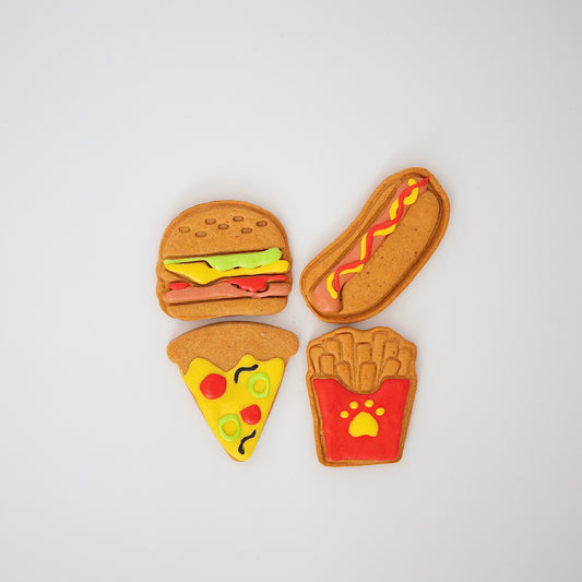 The Fast Food Pack by Macs Munchies includes four cookies shaped like a burger, hot dog, pizza slice, and fries. Decorated with vibrant K9-safe icing on a white base, these treats offer discerning pups a tasty peanut butter flavor twist!.