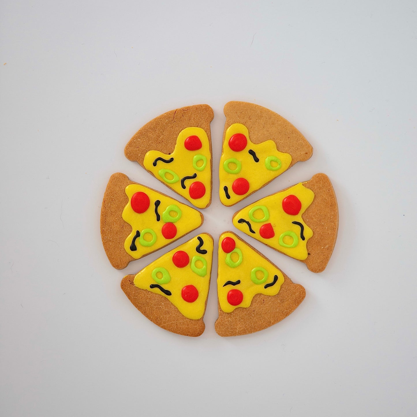 Six dog-friendly treats from Macs Munchies, shaped like pizza slices arranged in a circle, topped with K9-safe cheese icing, pepperoni circles, vegetable circles, and olive squiggles—create the perfect Pizza Pizza! delight.