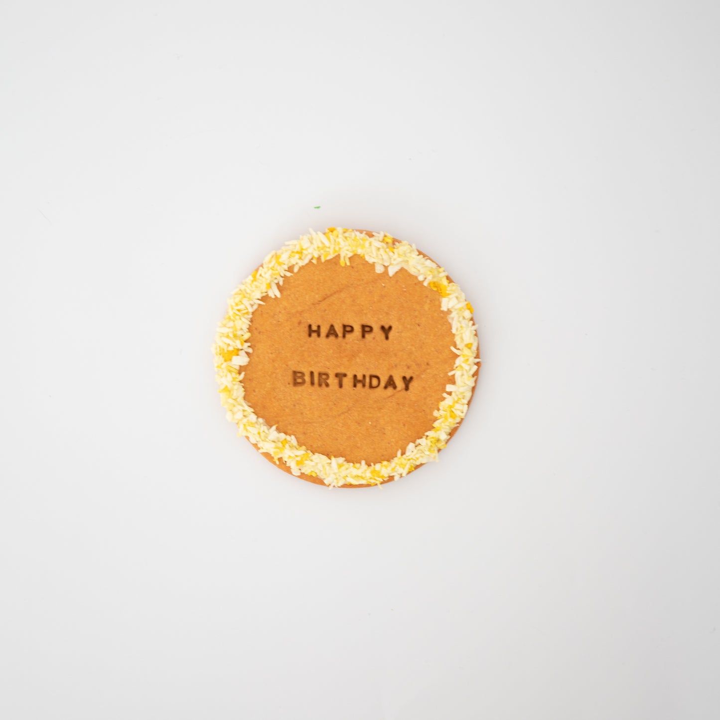 Macs Munchies XL Cookie is a round, hand-iced treat with HAPPY BIRTHDAY written on it and coconut sprinkles around the edge. Against a plain white background, its a perfect celebratory treat for your furry friends special day.