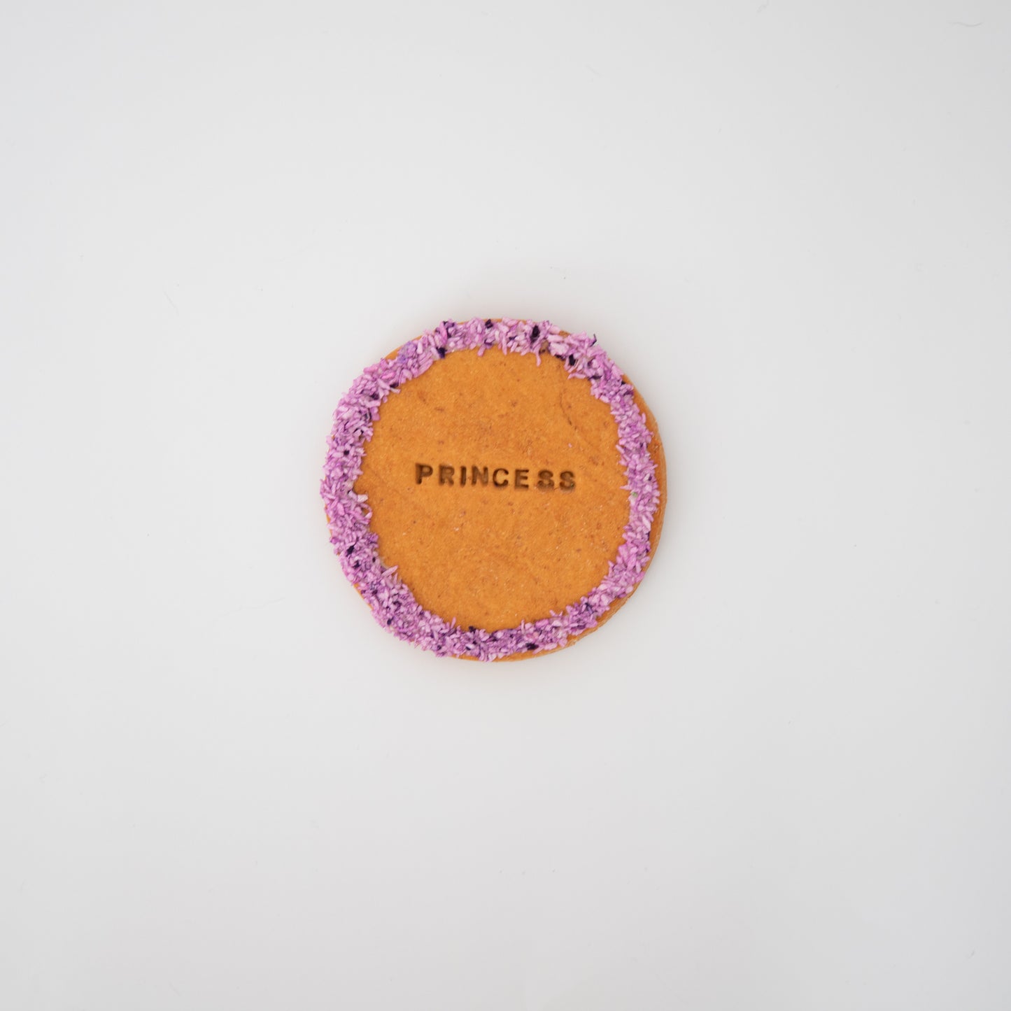 Macs Munchies presents the XL Cookie, a peanut butter-flavored biscuit adorned with purple sprinkles around the edge and stamped with PRINCESS in the center, set against a plain white background for taste and admiration.